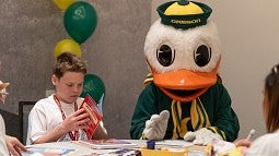 Picture of the Oregon Duck mascot sitting next to a younger person at a table