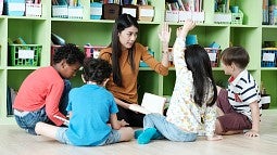 Image of a teacher sitting on the floor working with young students