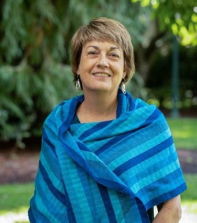 Picture of Lynn Stephen outside with green background and wearing a blue scarf